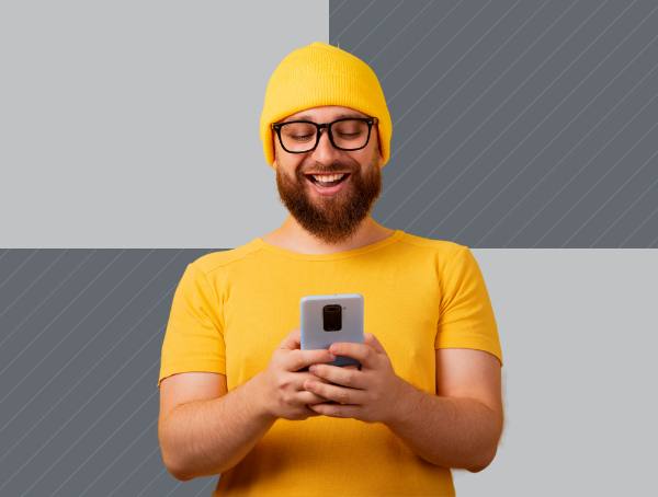 A man wearing a yellow shirt and hat smiles at his phone screen.