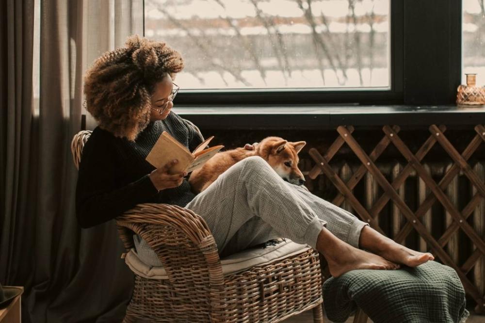 A woman curls up with a book and her dog in the wintertime